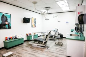 a large, open room contains two dental chairs and equipment sets, there's also a television mounted on the wall, benches with pillows for caregivers, and posters on the wall