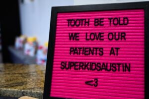 a bright pink sign board with the quote "tooth be told we love our patients at super kids austin"