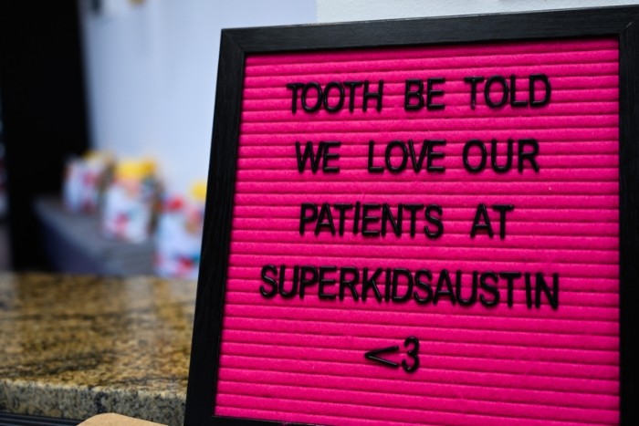 a bright pink sign board with the quote "tooth be told we love our patients at super kids austin"
