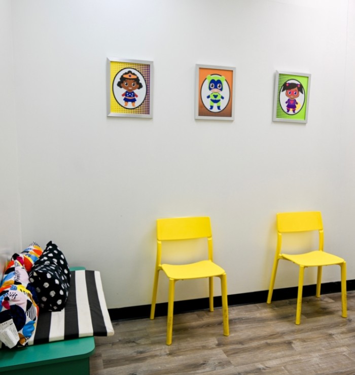 two yellow chairs and a bench with colorful cushions are inside the baby room
