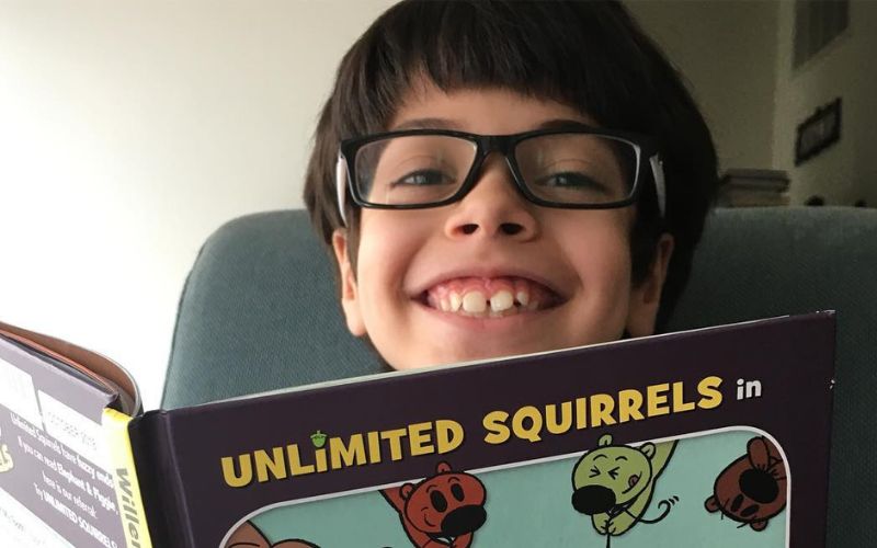 a boy with glasses and a large smile looks over a book titled "I lost a tooth"
