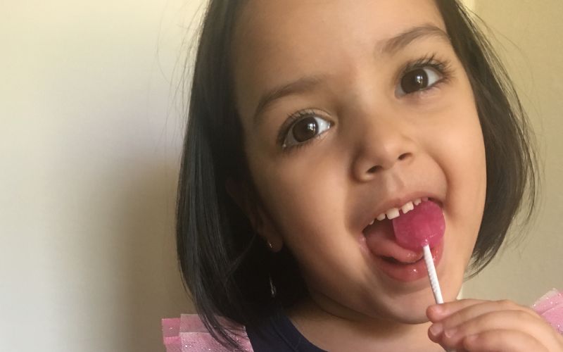 little girl licks red lollipop with a smile on her face