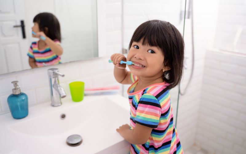 little girl brushes her teeth as she turns to look over her shoulder