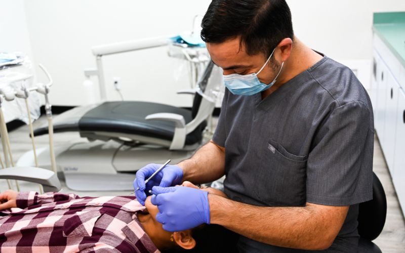 A male dentist wears a mask and gloves while looking into a child's mouth