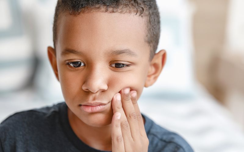 a young boy touches his cheek in apparent pain