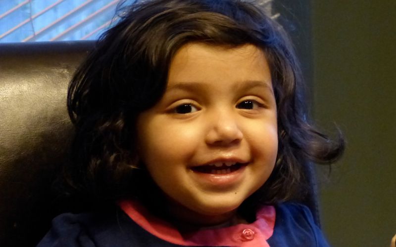 A small girl with round cheeks and curly hair smiles at the camera