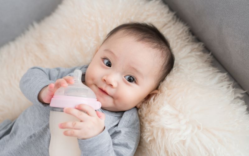 infant holds a bottle while looking to the side