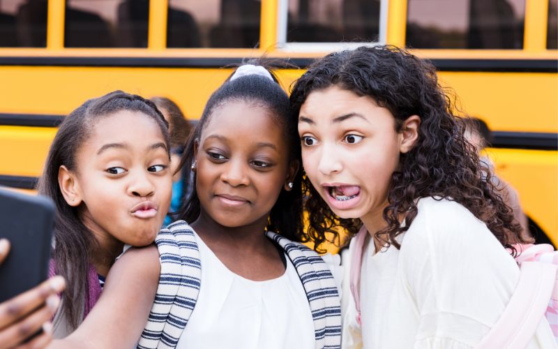 three tween aged girls make silly faces and smile while taking a selfie