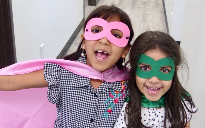 two girls dressed as superheroes smile in the hallway