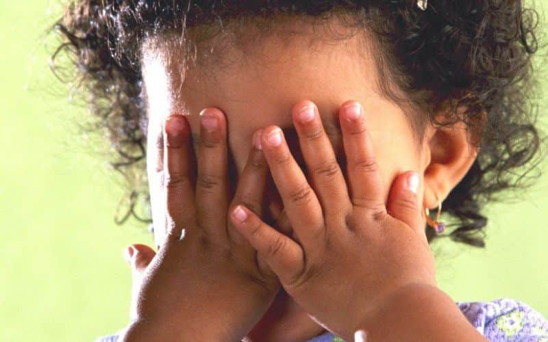 A small girl hides behind her hands