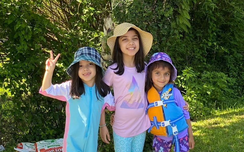Three girls stand under a palm tree and smile at the camera